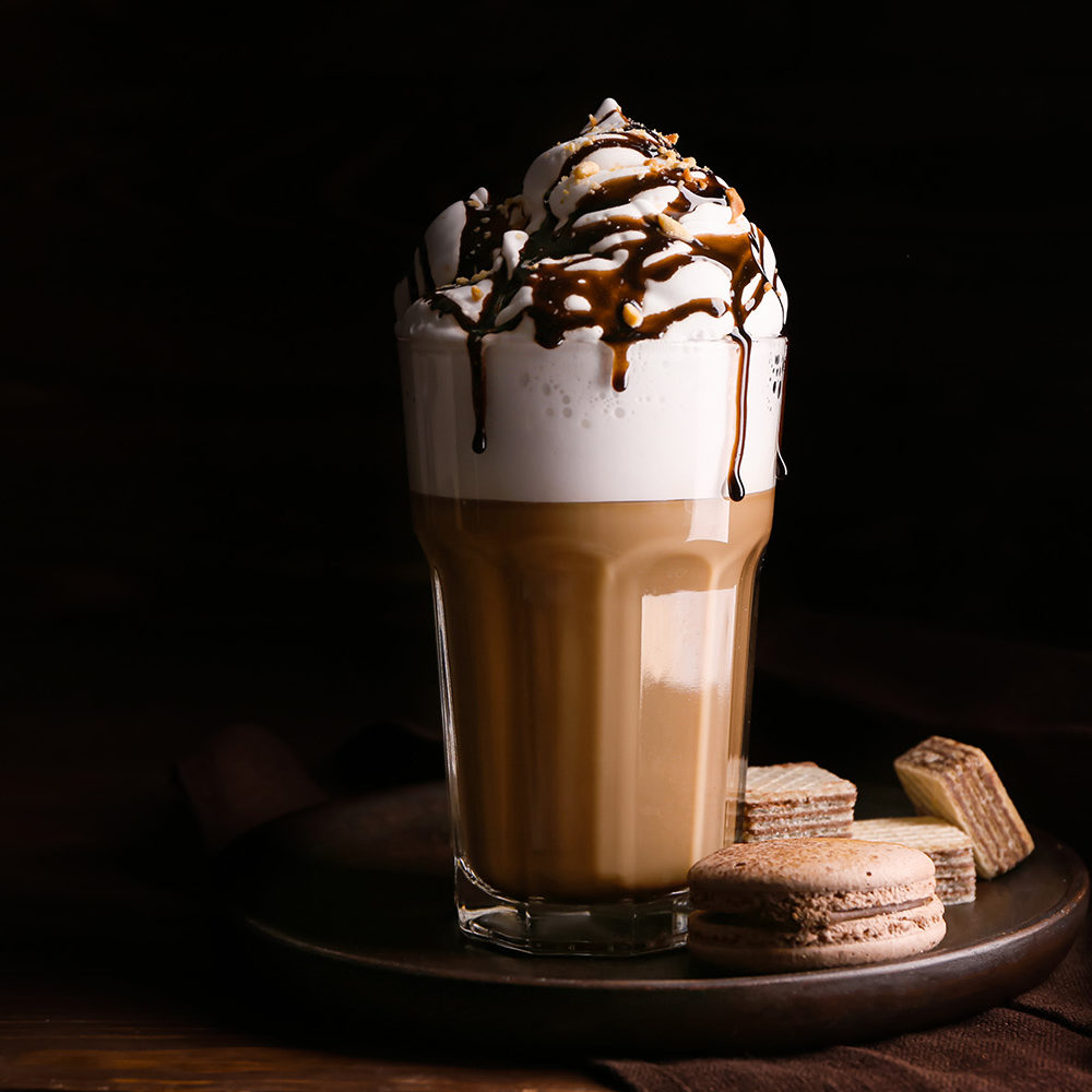 Glass of tasty frappe coffee with sweets on wooden table